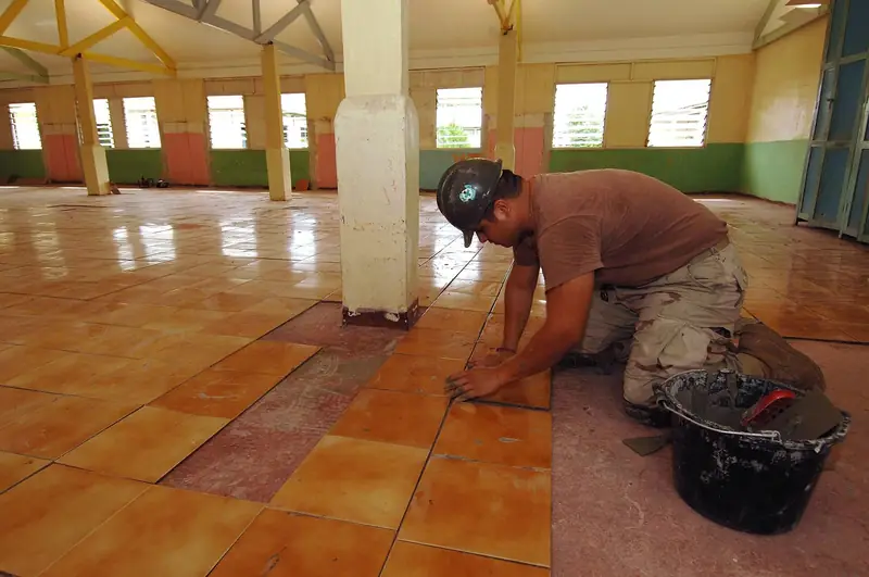 Carreleur à genoux qui pose de grands carreaux de terre cuite orangés